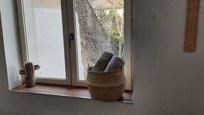 Ein Fenster mit einem gewebten Korb, der Handtücher, einen kleinen Kaktus und ein dekoratives Objekt auf einer Holzablage enthält.