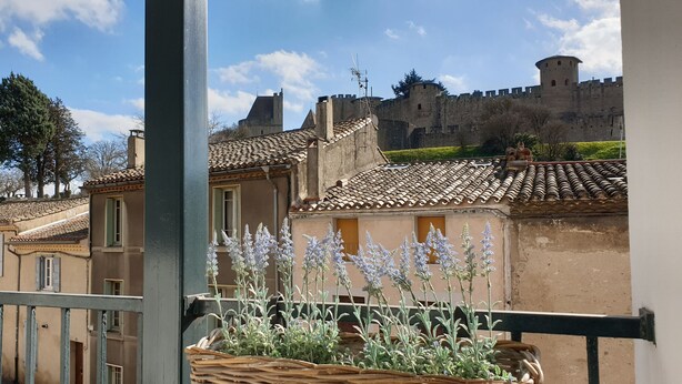 Ein Balkon mit Blick auf ein Schloss, Gebäude mit Terrakotta-Dächern und ein Lavendelgarten.