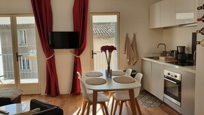 Eine moderne Küche mit Flachbildfernseher, Essbereich mit weißen Stühlen und einem runden Tisch sowie ein Balkon mit roten Vorhängen.