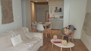 Ein Wohnzimmer mit einer Couch, Sesseln, einem kleinen Tisch und einer sichtbaren Küchenzeile im Hintergrund.
