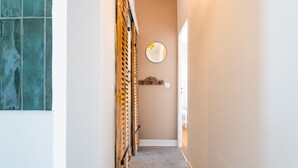 A narrow hallway with a wooden lattice door, a round mirror on the wall, and a carpeted floor.