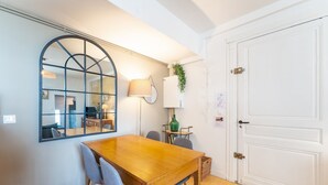 A dining area with a wooden table, two chairs, a mirror, a lamp, and a door.