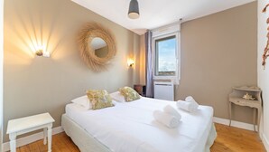 A bedroom with a large bed, bedside tables, a window with curtains, a wall-mounted mirror, and a hanging light fixture.