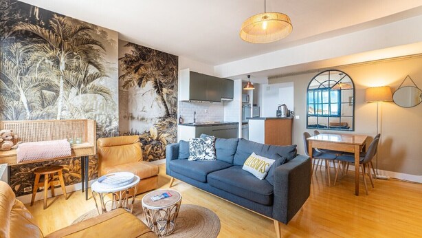A modern living room with a blue sofa, wooden coffee table, and a dining area with a wooden table and chairs.