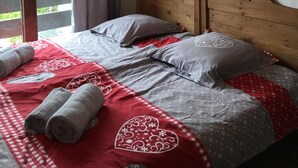 A bedroom with a wooden headboard, a bed with patterned bedding, a window with curtains, and wall-mounted lamps. - Apartment 4/6 pers, 50m², Les Houches Chamonix (Les Houches)