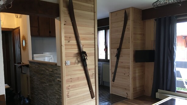 A modern interior with wooden walls, a stone accent wall, a kitchen area, and a seating area with a table and chairs. - Apartment 4/6 pers, 50m², Les Houches Chamonix (Les Houches)