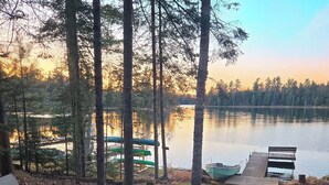 A lakeside deck with chairs, a fire pit, and a dock with boats. - Lake Days, Bonfires
& Cabin Nights
2 Bedrooms / 2 Bathrooms  (Boulder Junction)