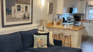 Een moderne woonkamer met een donkerblauwe bank, een houten salontafel en een keuken op de achtergrond.
