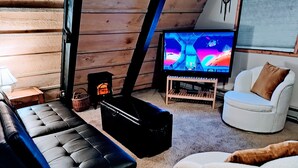A cozy living room with a black leather sofa, a white armchair, a small wooden table, and a television displaying a colorful scene.