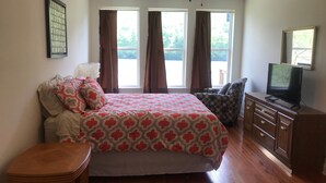 A bedroom with a bed, a TV, a dresser, and two windows with curtains.