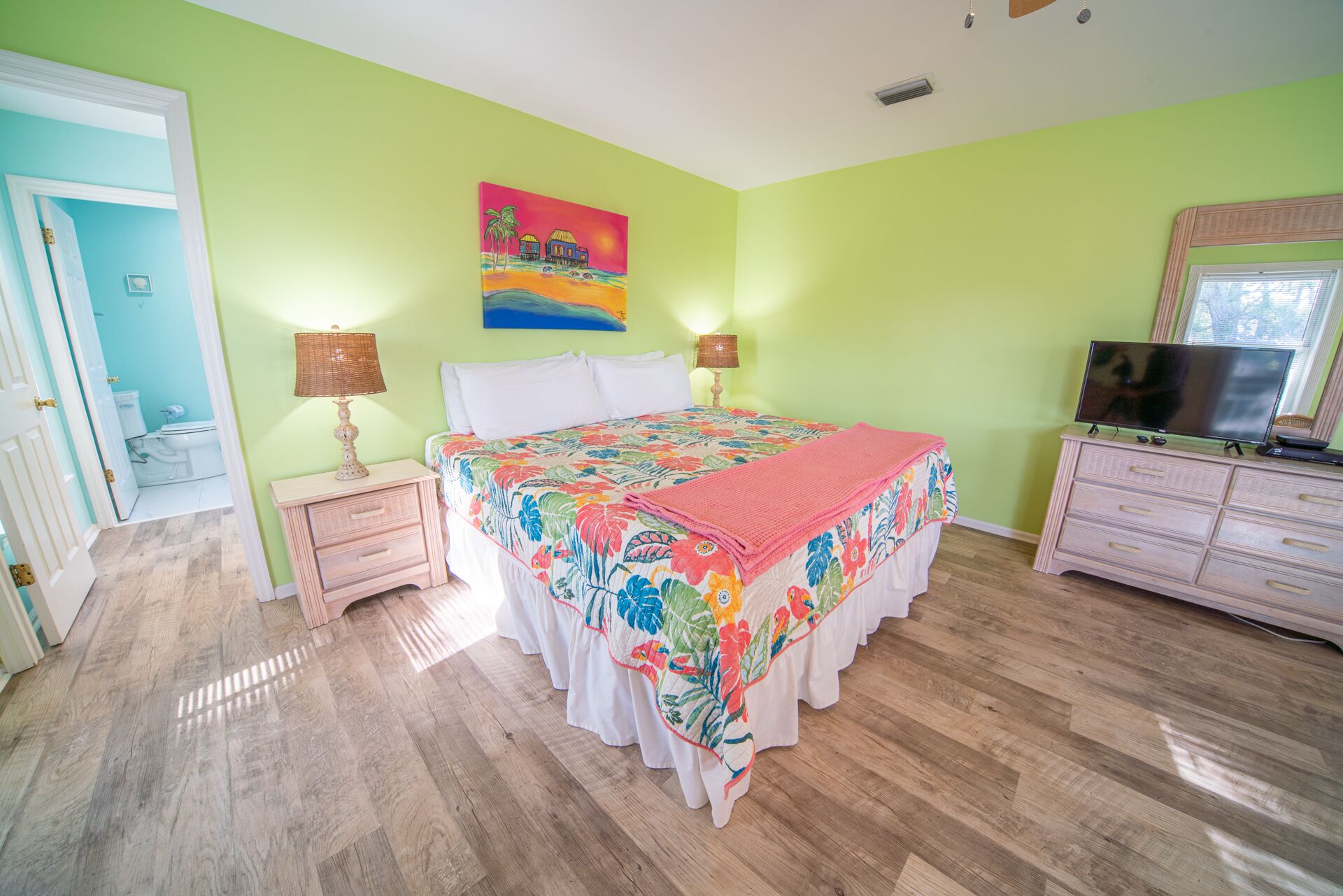 A bedroom with a bed, bedside lamps, a dresser, a television, and a painting on the wall.