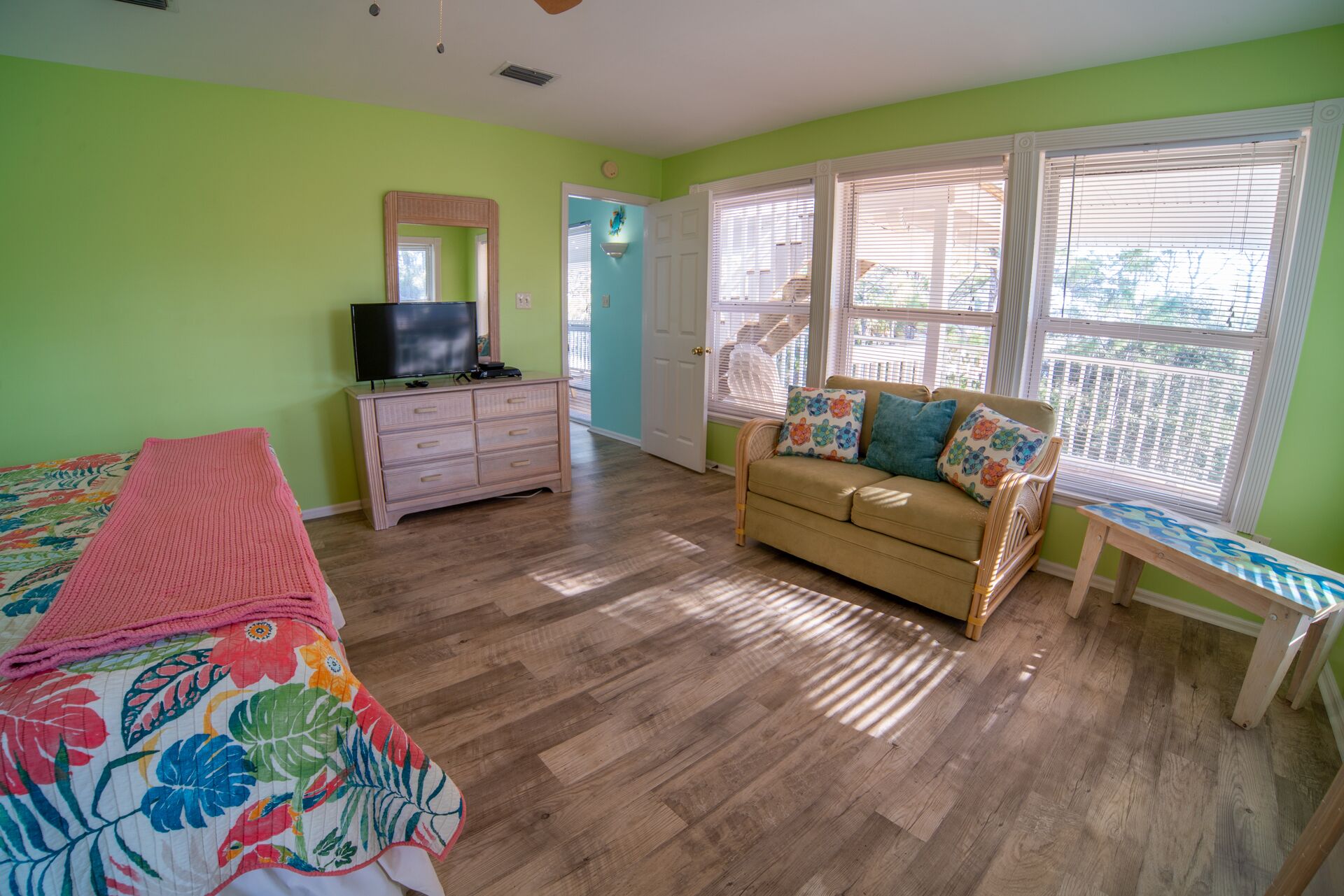 A bedroom with a bed, a dresser, a television, a sofa, and a window with blinds.