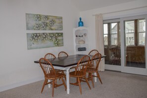A dining room with a dark wooden table and six wooden chairs, a white shelf with decorative items, and two floral paintings on the wall.