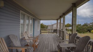 Ett trädäck med Adirondack-stolar, en inglasad veranda och utsikt över ett bostadsområde.