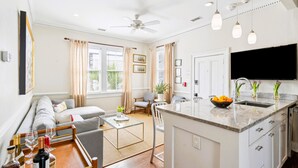 A modern kitchen with a central island, a dining area with a sofa and chairs, and a living room with a sofa and a coffee table. - 8D at Saint Philip Square, One Block to King, Top Floor Apt with Private Balcony (Charleston)