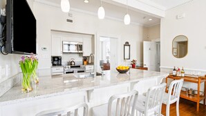 A modern kitchen with white cabinetry, a central island with bar stools, a microwave, stove, and a sink. - 8D at Saint Philip Square, One Block to King, Top Floor Apt with Private Balcony (Charleston)