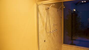 A glass-enclosed shower with a handheld showerhead and a wall-mounted faucet.