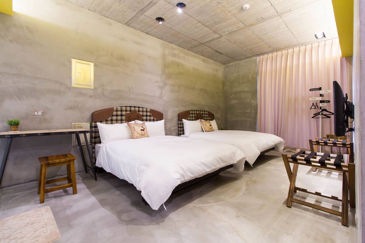 A bedroom with a bed, a desk, a chair, and a small stool.