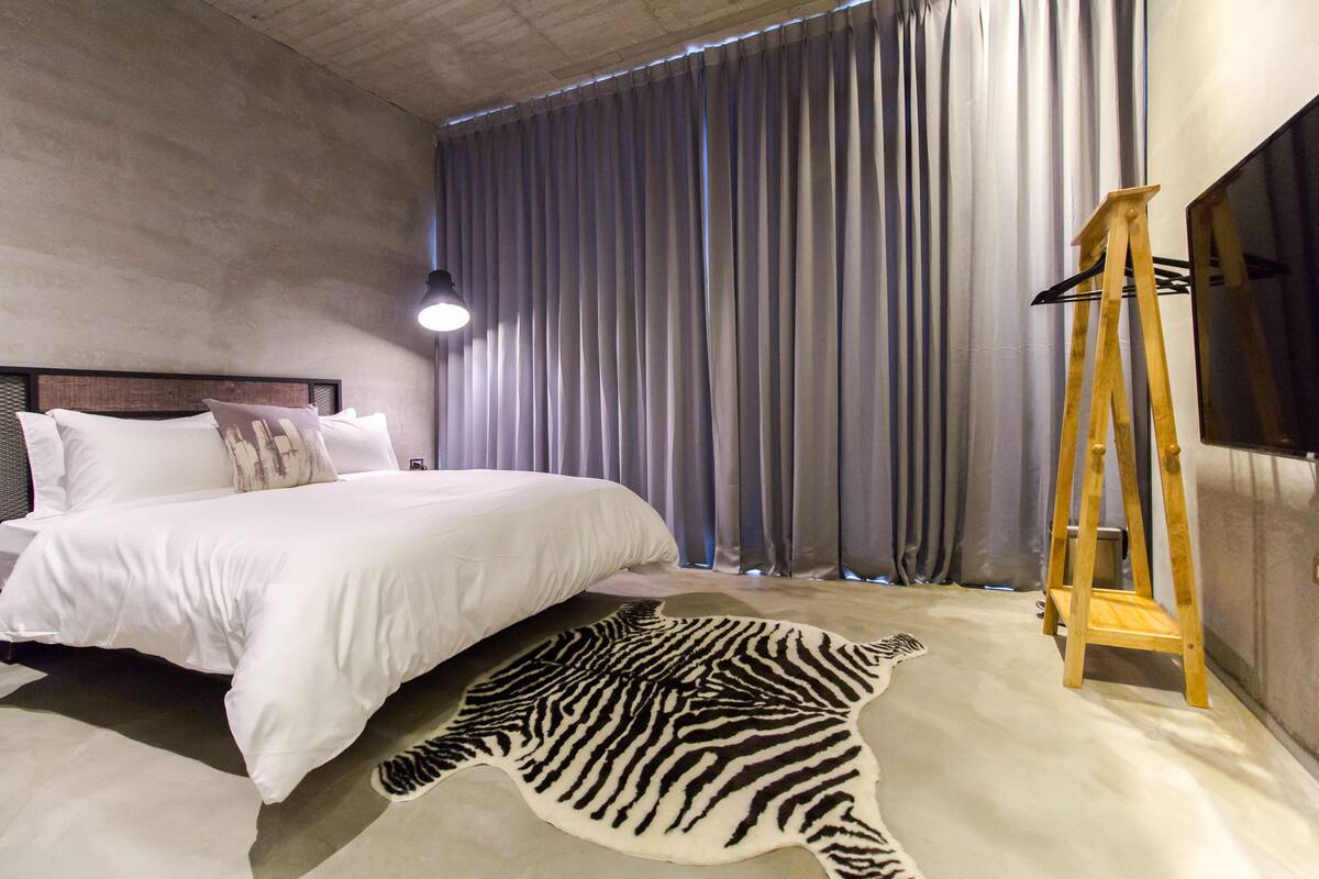 A bedroom with a large bed, grey curtains, a zebra rug, and a wooden ladder.