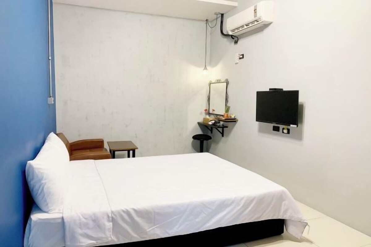 Habitación de hotel con cama, escritorio con silla, espejo y televisor de pantalla plana.