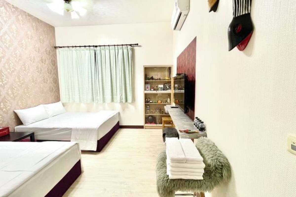 Una habitación pequeña con cama, una mesita, un estante con adornos y un banco cubierto de piel.