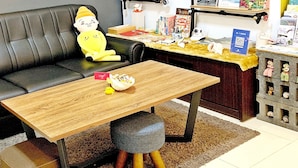 A black leather sofa with a yellow plush toy, a wooden coffee table, and a small stool. - Snug Nine Inn (Hengchun)