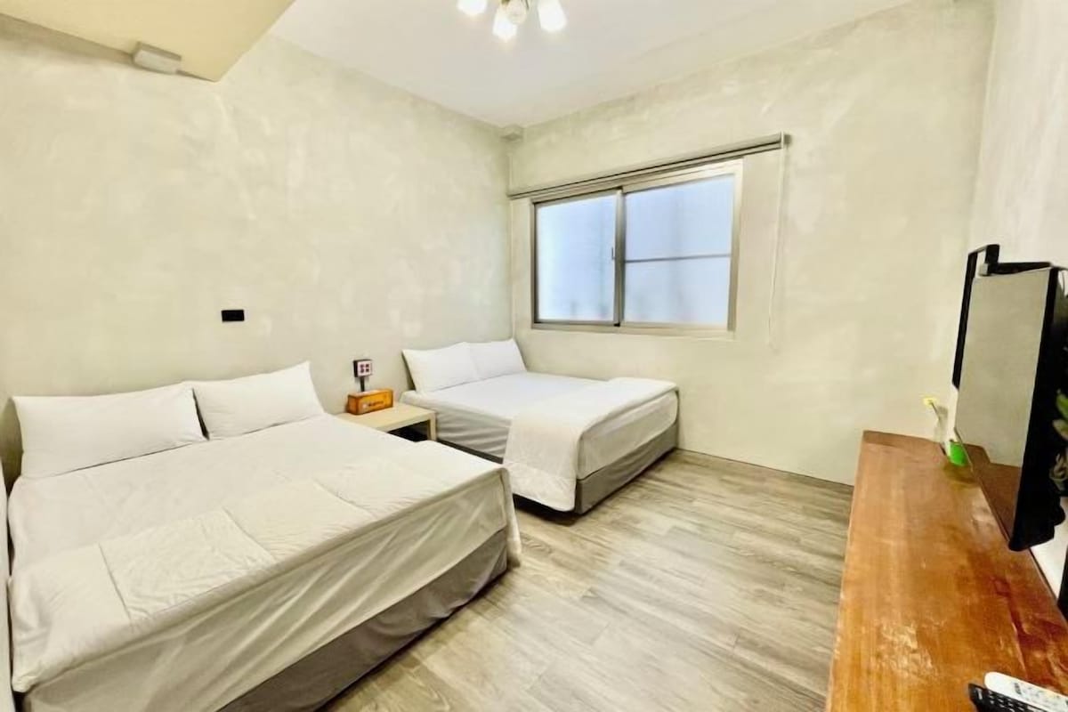 Una habitación con dos camas, un escritorio de madera, una ventana y un televisor montado en la pared.