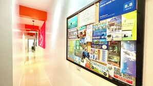 A corridor with a bulletin board displaying various travel-related posters and signs, including a map and a QR code. - Snug Nine Inn (Hengchun)