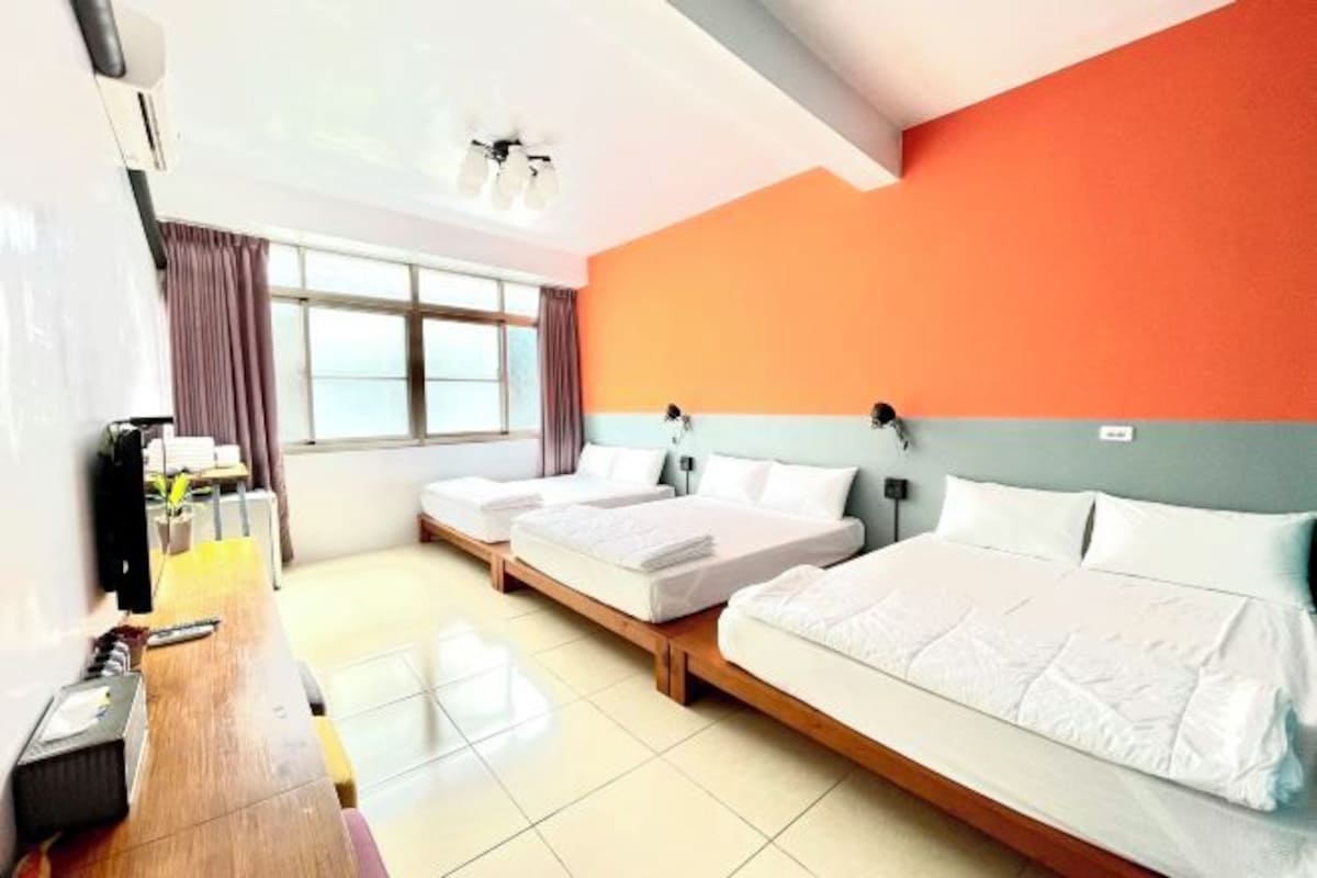 A hotel room with two single beds, a wooden desk, a large window, and a view of the sea.