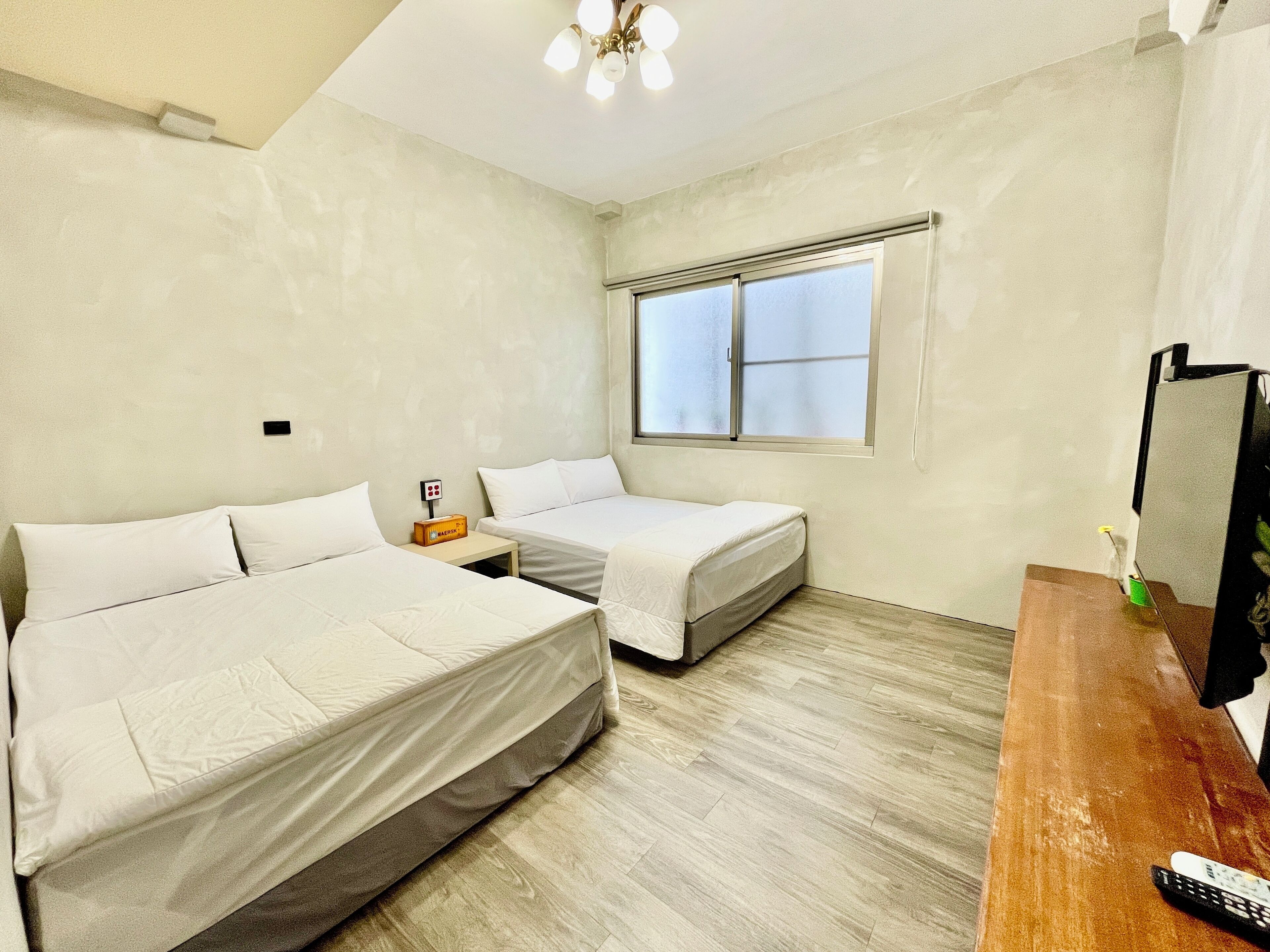 A room with two beds, a wooden dresser, a TV, and a window with blinds.
