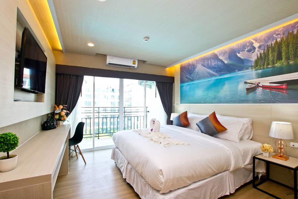 A hotel room with a large bed, a TV mounted on the wall, a desk with a plant, and a view of a lake with boats.