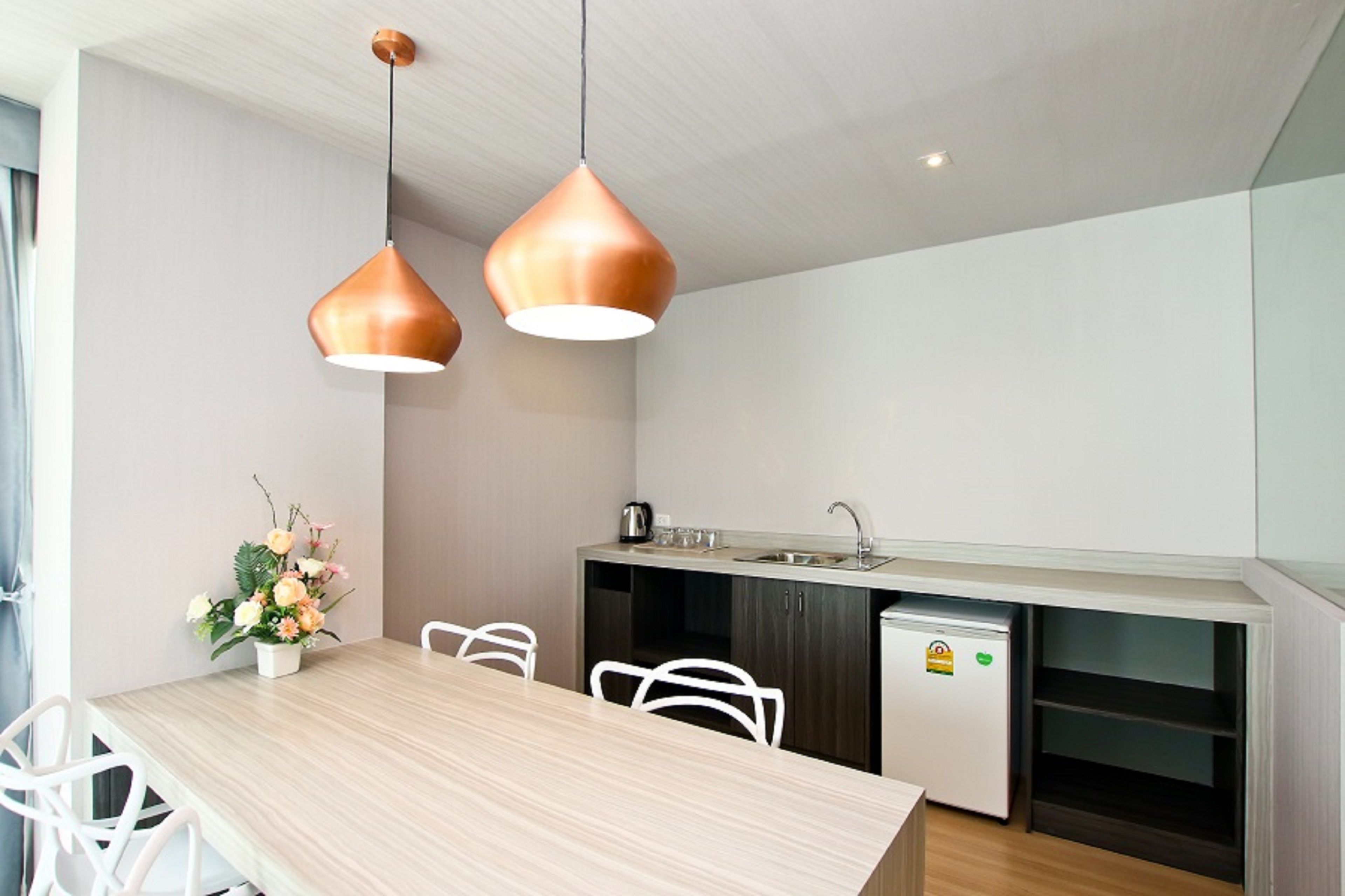 A modern kitchen with a wooden table, white chairs, and two copper pendant lights.