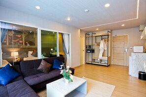 A modern living room with a dark-colored sofa, a white coffee table with a floral arrangement, and a large window with curtains. - Le Breeze Resort Hua Hin (Cha-am)