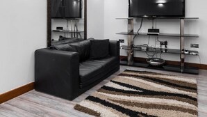 Uma sala de estar moderna com um sofá de couro preto, uma televisão de tela plana em uma prateleira de vidro e um espelho grande na parede.