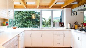 A modern kitchen with white cabinets, a large window, and a view of greenery outside. - National Award Winner with Stunning View (Havelock North)