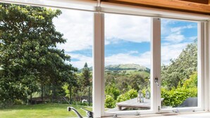 A kitchen with a large window offering a view of a green landscape and hills. - National Award Winner with Stunning View (Havelock North)