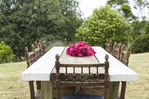 Une table à manger en bois, recouverte d’une nappe blanche et agrémentée d’un centre de table floral, entourée de chaises aux pieds et au dossier en bois.