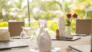 A table set for dining outdoors with clear glassware, napkins, and a vase with flowers. - Hotel Rudi (Nairobi)