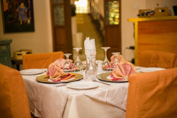 Une table à manger dressée avec des assiettes, des serviettes et de la verrerie, entourée de chaises.