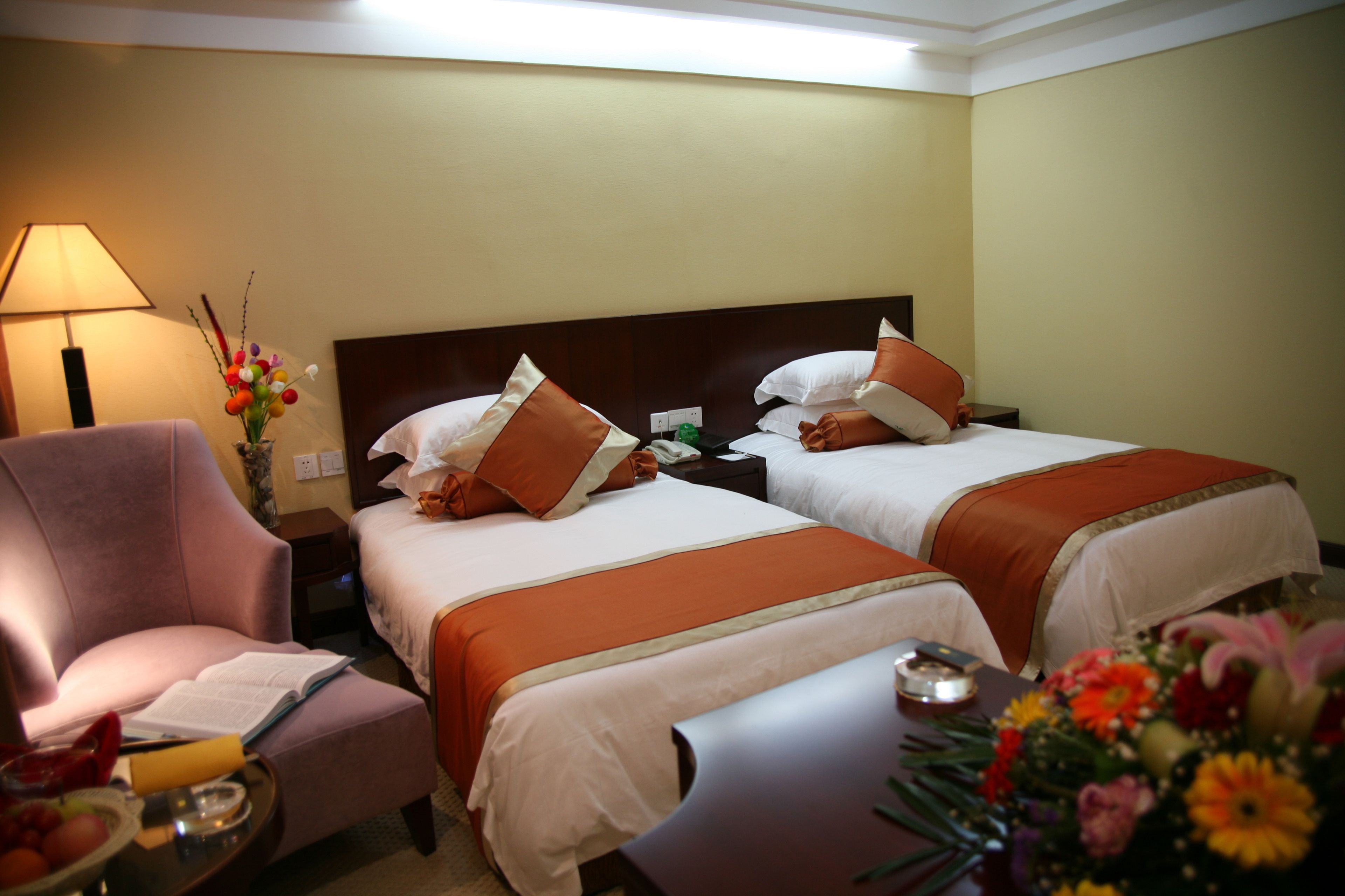 A hotel room with two beds, a desk, a chair, a lamp, and a vase of flowers.