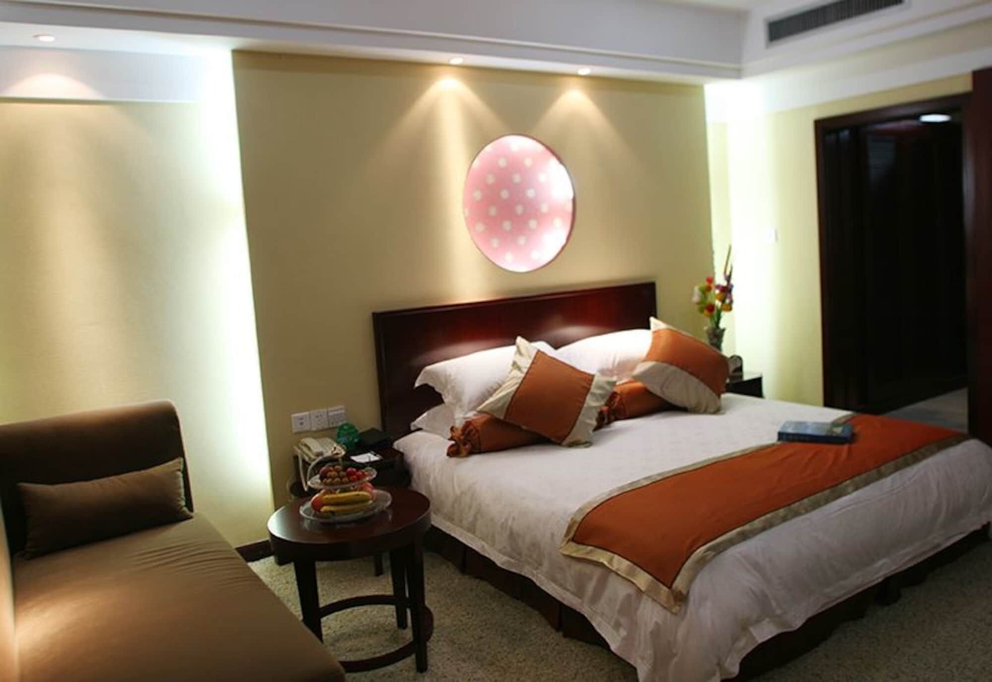 A hotel room with a bed, a sofa, a small table with fruits, and a wall-mounted circular decoration.