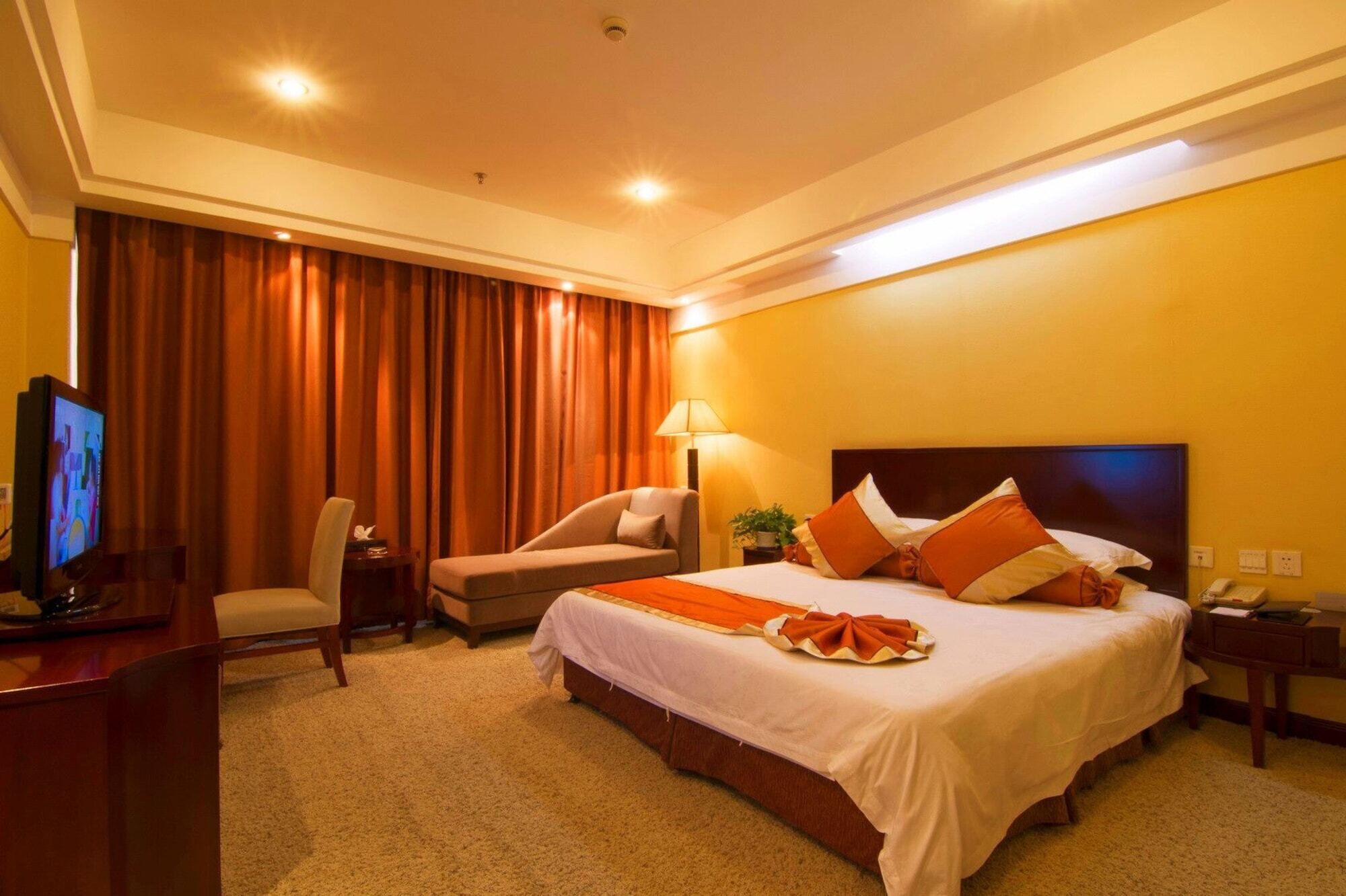 Une chambre d’hôtel avec un lit, un bureau, une chaise, une télévision et une lampe.