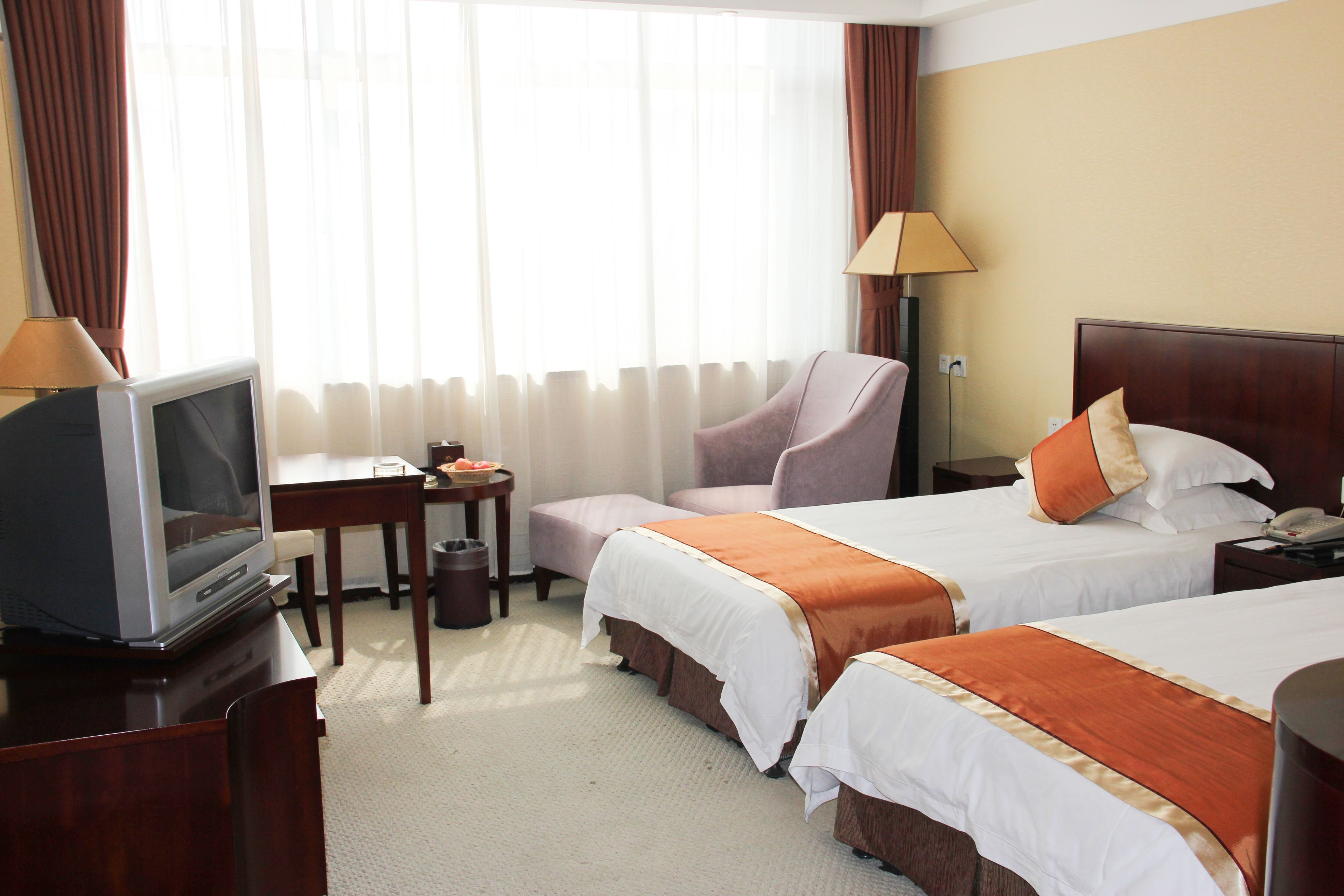 A hotel room with two beds, a desk with a television, a chair, and a lamp.