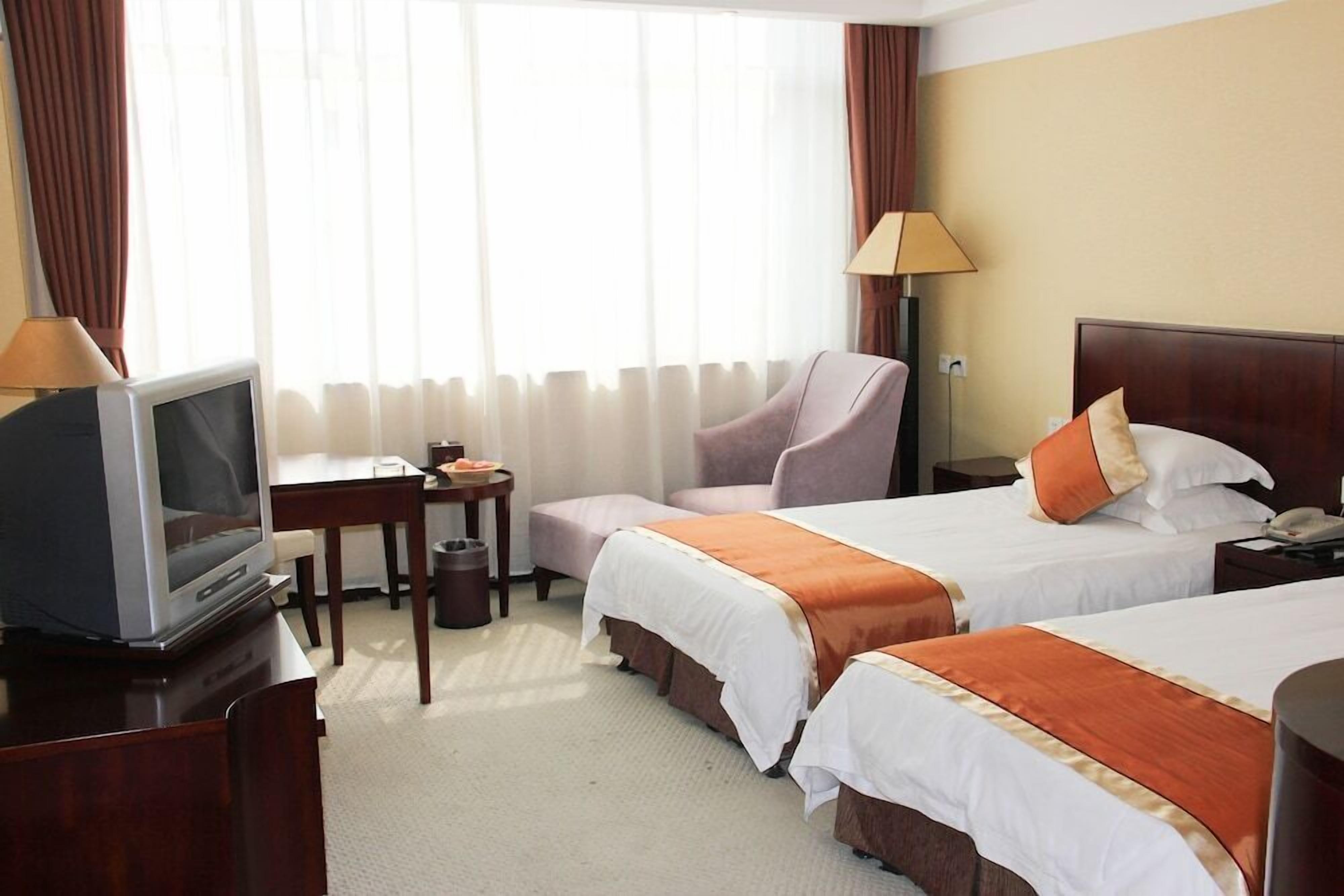 A hotel room with two beds, a desk, a television, and a lamp.
