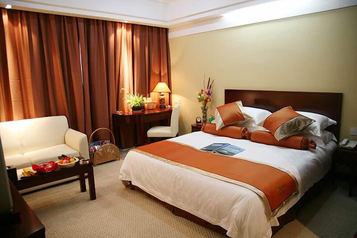 A hotel room with a large bed, a sofa, a desk with a lamp, and a vase with flowers.