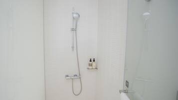 Een badkamer met een glazen douchecabine, een handdouche en een wandmengkraan.