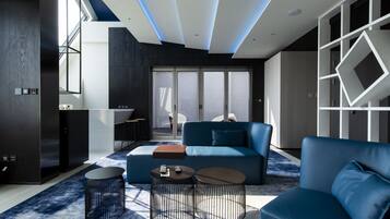 Una sala de estar moderna con un sofá azul, dos mesas redondas y un amplio ventanal.