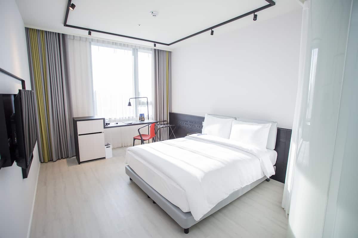 A modern hotel room with a large bed, a desk, and a chair.