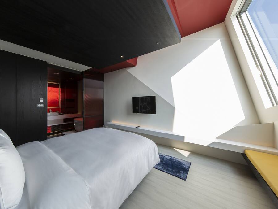 Un dormitorio moderno con una cama grande, un escritorio y una habitación roja al fondo.