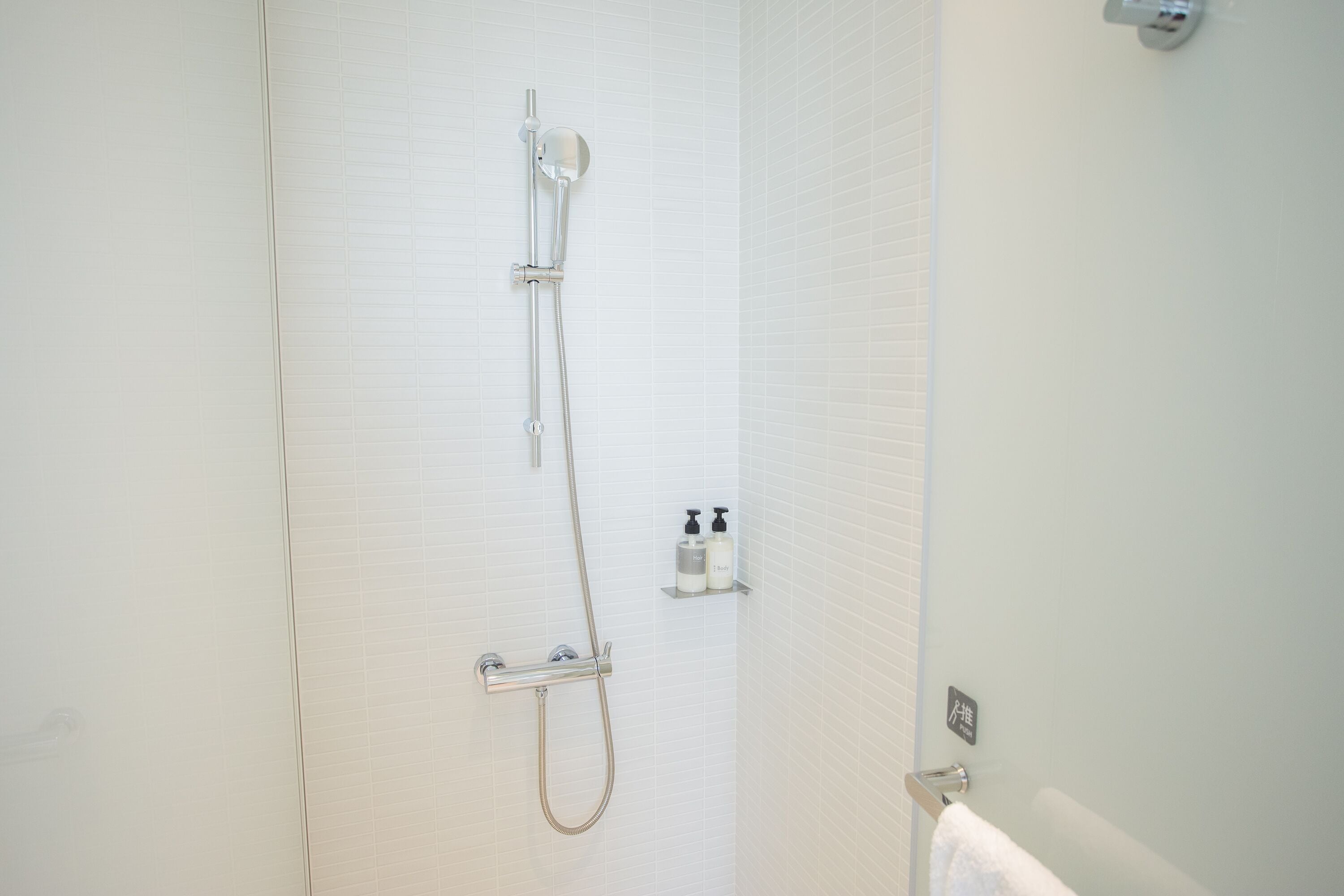 Un baño con ducha, un perchero y un dispensador de jabón en la pared.